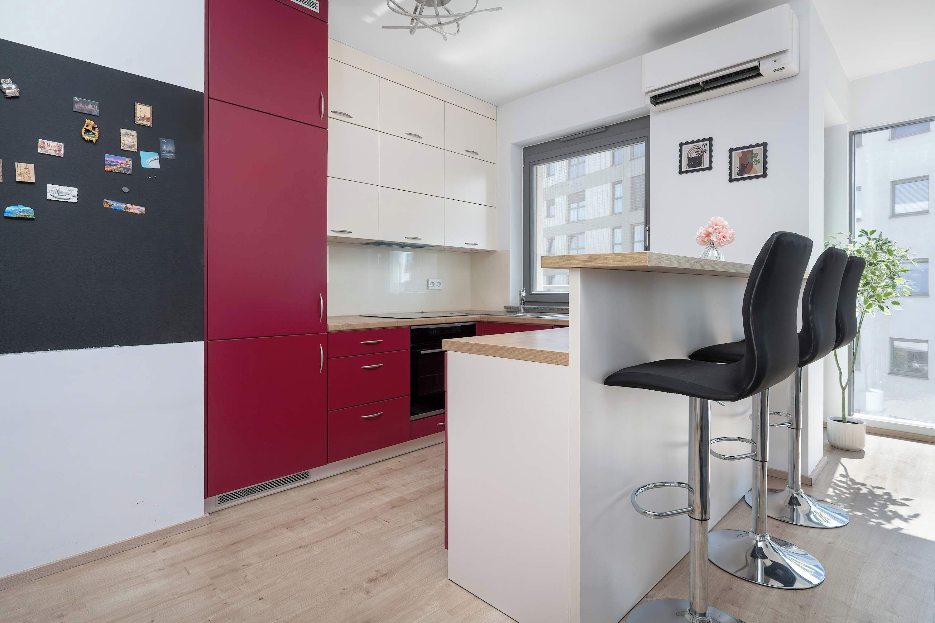 A modern kitchen with red and white cabinetry, a built-in oven, and a bar area with a stool.
