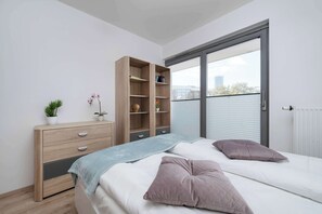 Ein Schlafzimmer mit einem Bett, einer Kommode, einem Bücherregal und einem großen Fenster.