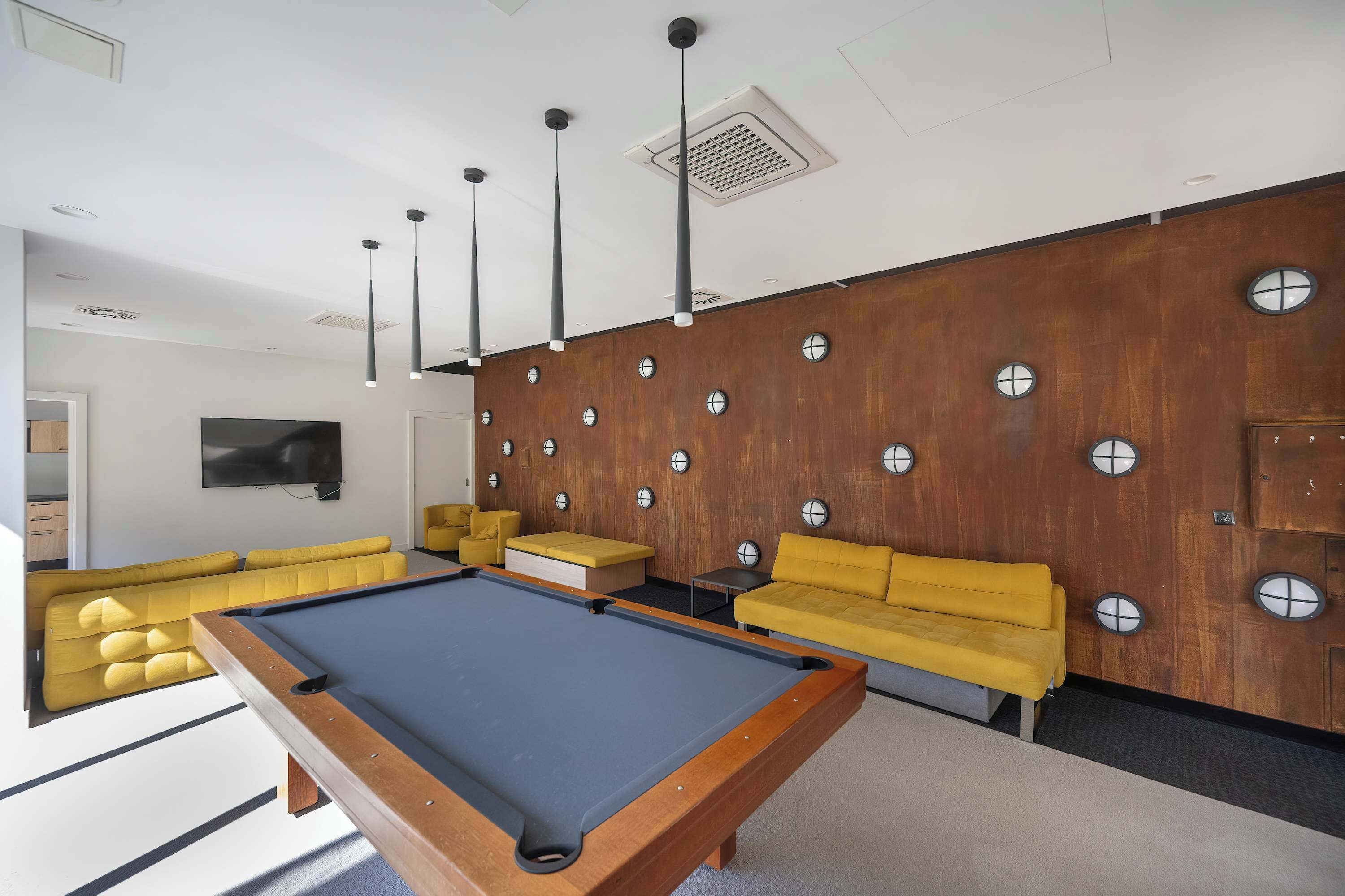 A modern lounge area with a pool table, yellow sofas, and a television.