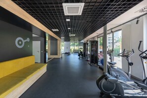 Ein Fitnessraum mit Trainingsgeräten, einer gelben Bank und einem großen Fenster.