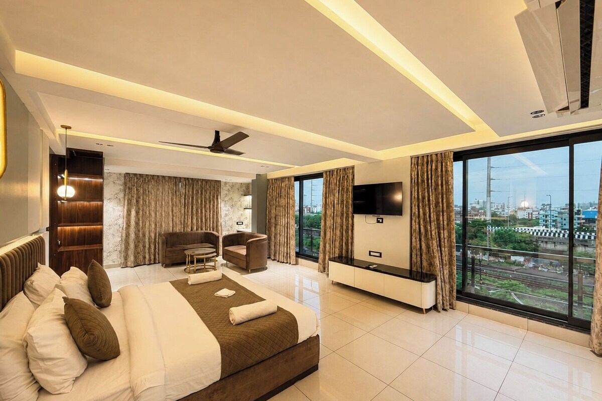 A modern hotel room with a large bed, a seating area, a flat-screen TV, and a city view.