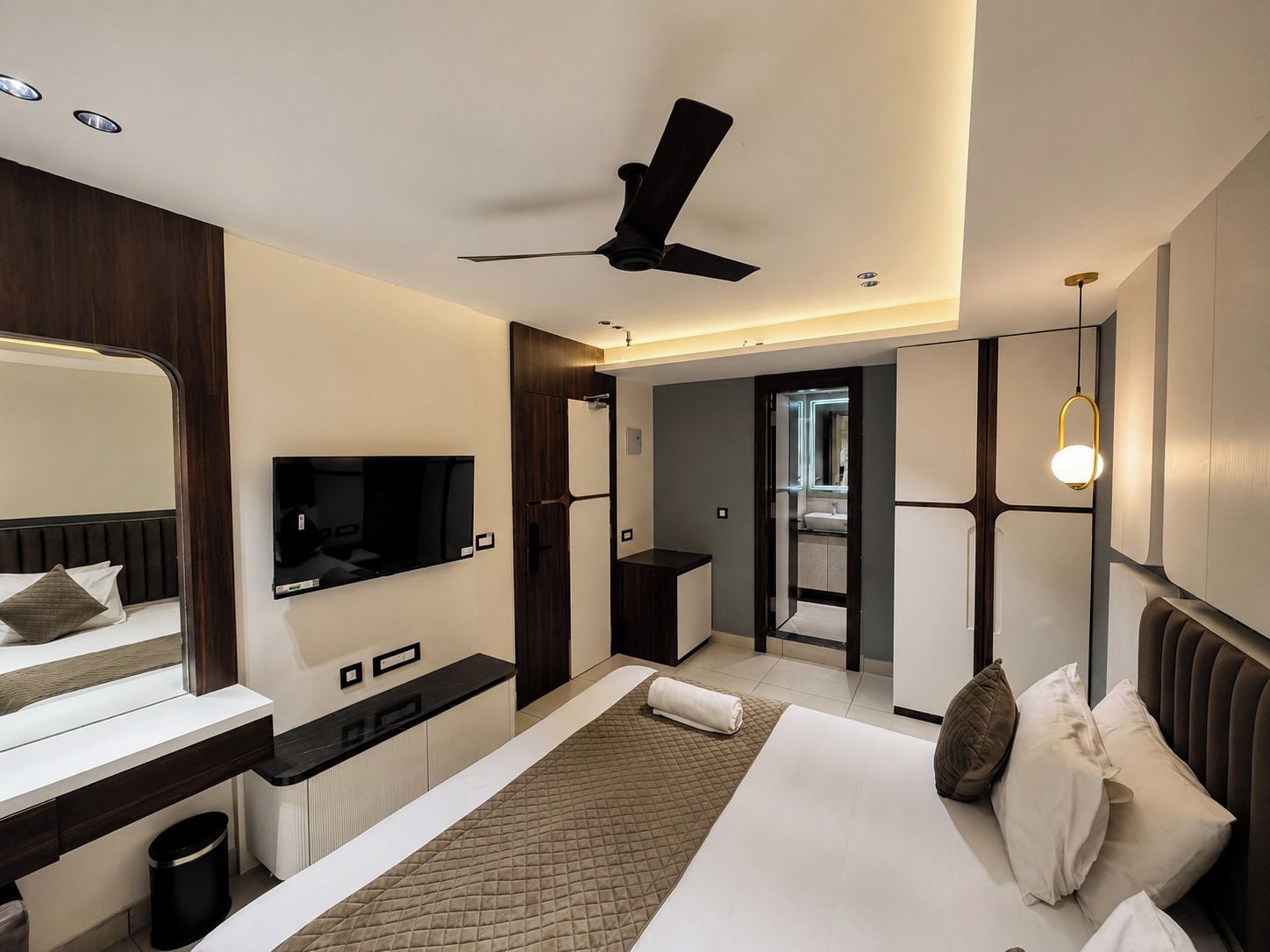 Quarto de hotel moderno com uma cama, televisão, ventoinha no teto e banheiro visível por uma porta aberta.