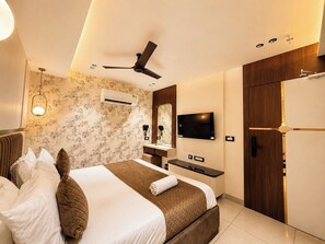 A hotel room with a bed, a desk, a TV, a wardrobe, and a ceiling fan. - HOTEL ROYAL GANGA (Patna)