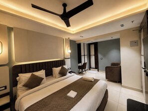 Una habitación de hotel moderna con una cama grande, un ventilador de techo y una zona de estar con una silla y una mesita.