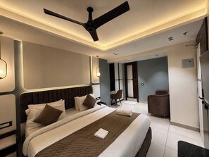 A modern hotel room with a large bed, a ceiling fan, and a seating area with a chair and a small table. - HOTEL ROYAL GANGA (Danapur)
