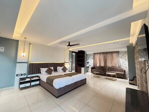 A modern bedroom with a large bed, a sofa, a TV, and a ceiling fan. - HOTEL ROYAL GANGA (Patna)
