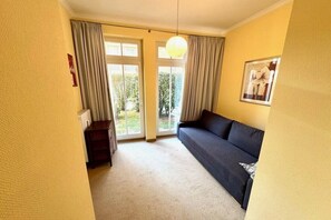 Ein Zimmer mit einer Couch, einem kleinen Tisch und einem Fenster mit Vorhängen.