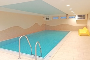 An indoor swimming pool with a tiled floor, a metal pool ladder, and a yellow poolside chair. - Holiday apartment Dünenschloss 319669 (Kühlungsborn)