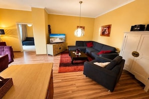 A living room with a sofa, coffee table, and a TV. There is a wooden cabinet and a red rug. - Holiday apartment Dünenschloss 319669 (Kühlungsborn)