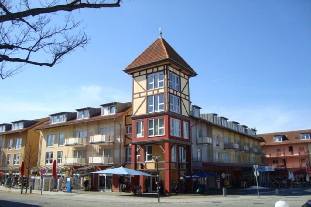 Un immeuble à plusieurs étages, doté d’une tour imposante, de balcons et d’un espace commercial au rez-de-chaussée avec une terrasse.