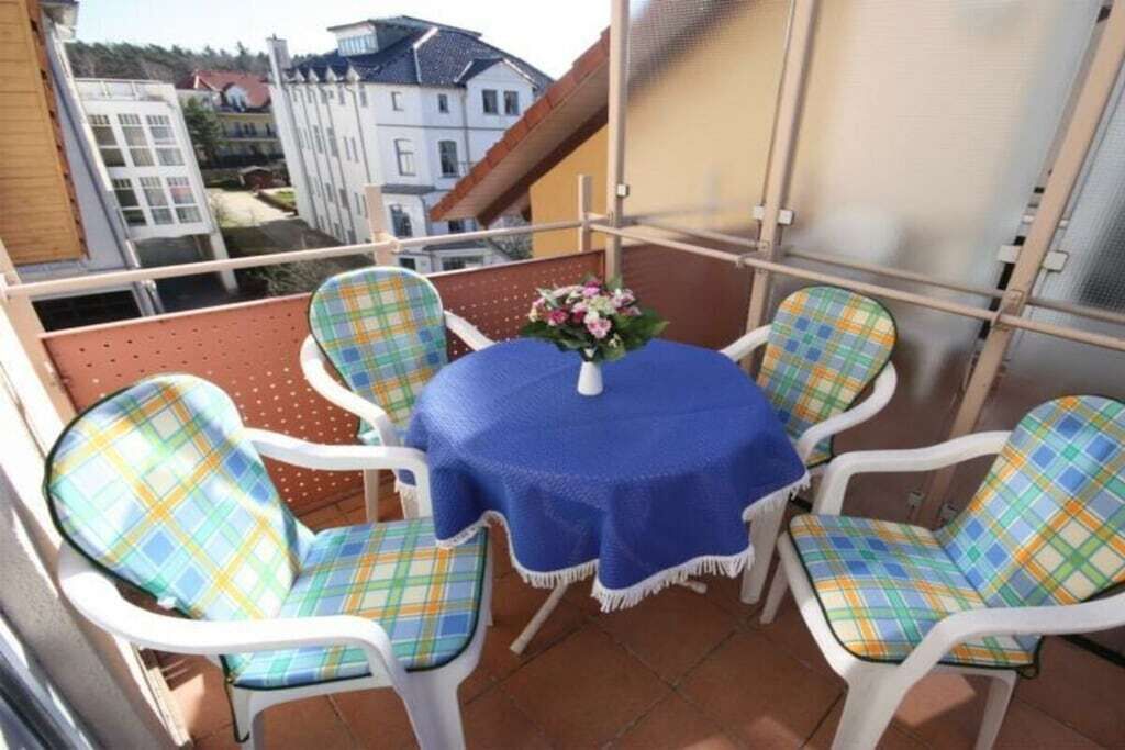 Un balcon avec une table ronde et quatre chaises, chacune agrémentée d’un coussin à carreaux.