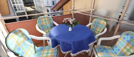 Un balcon avec une table ronde et quatre chaises, chacune agrémentée d’un coussin à carreaux.