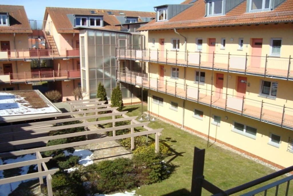A multi-story residential building with balconies, a covered outdoor area, and a garden.
