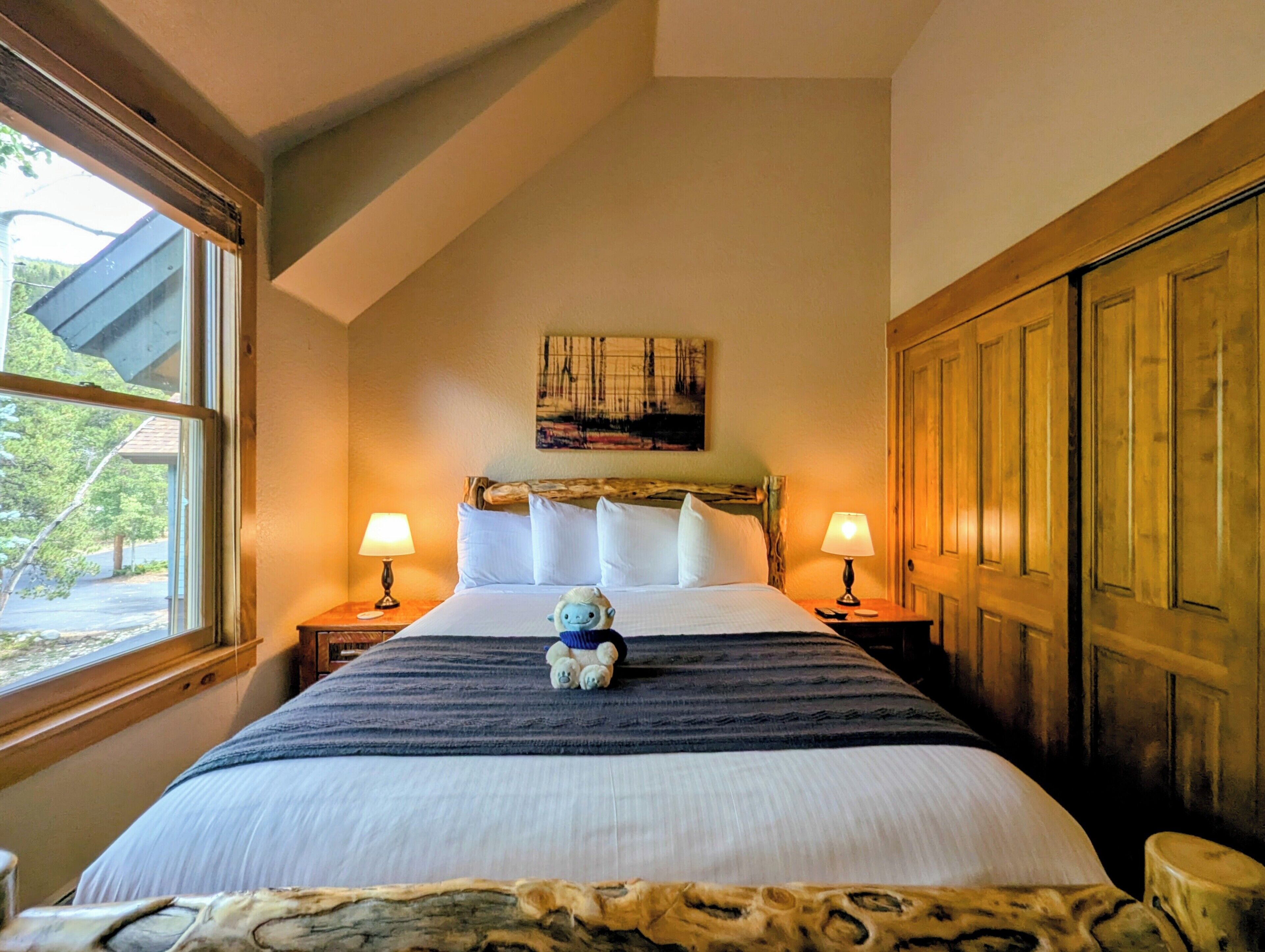 A bedroom with a bed, two bedside lamps, a window, and a wooden door.