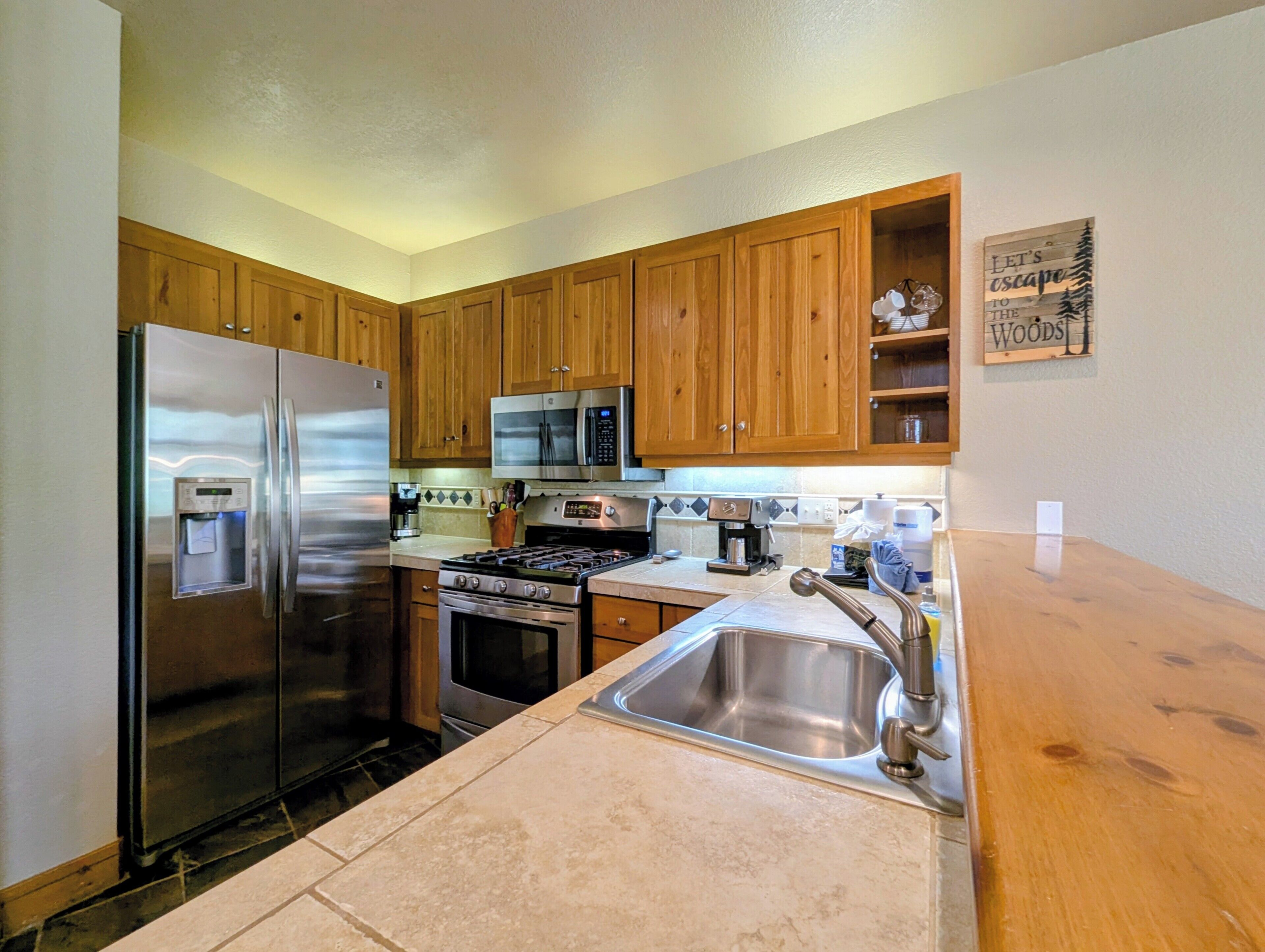 Una cocina con armarios de madera, electrodomésticos de acero inoxidable, microondas integrado y un lavabo.
