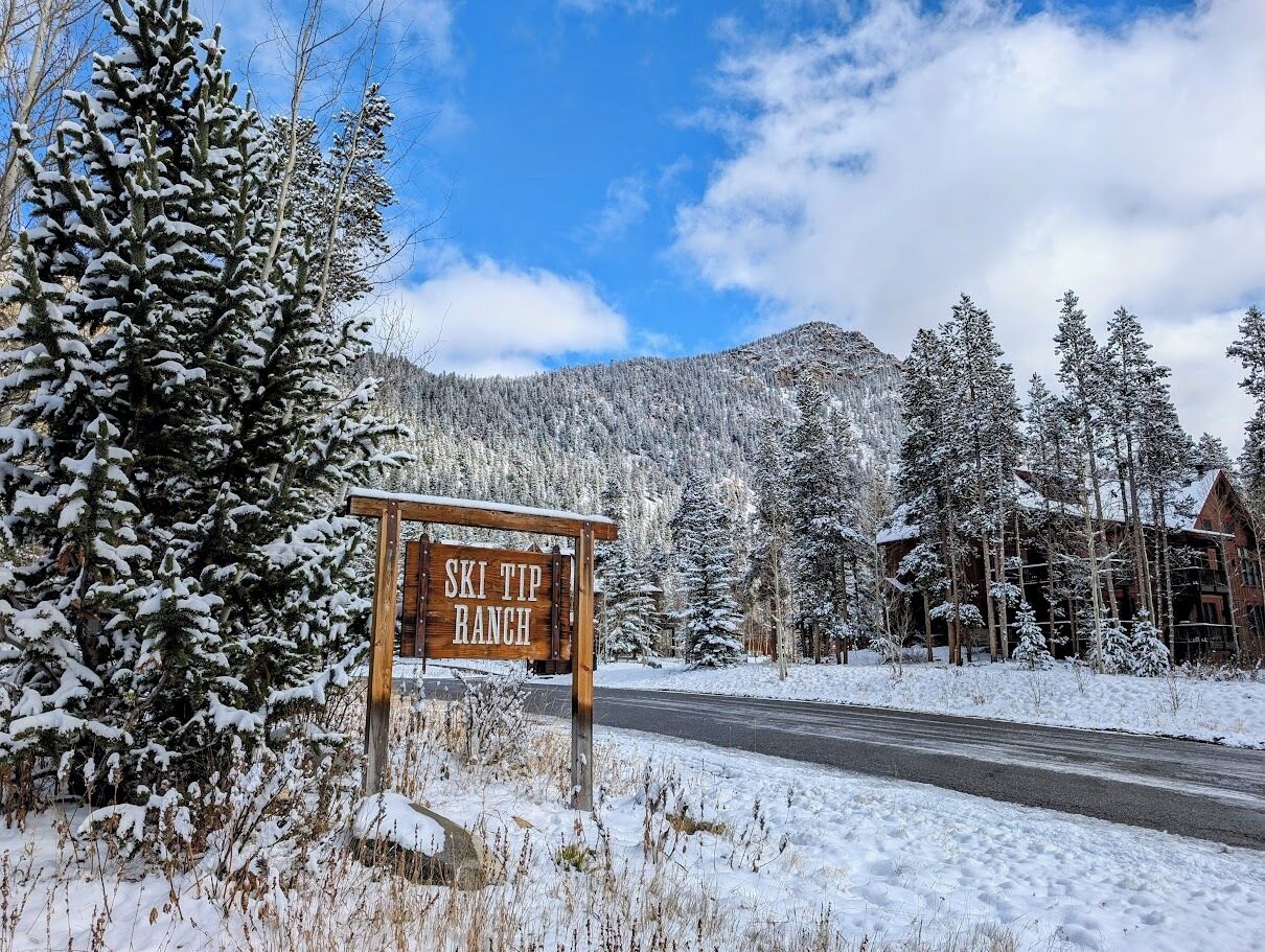 A wooden sign reading "SKI TIP RANCH" in a snowy landscape with a road and trees.
