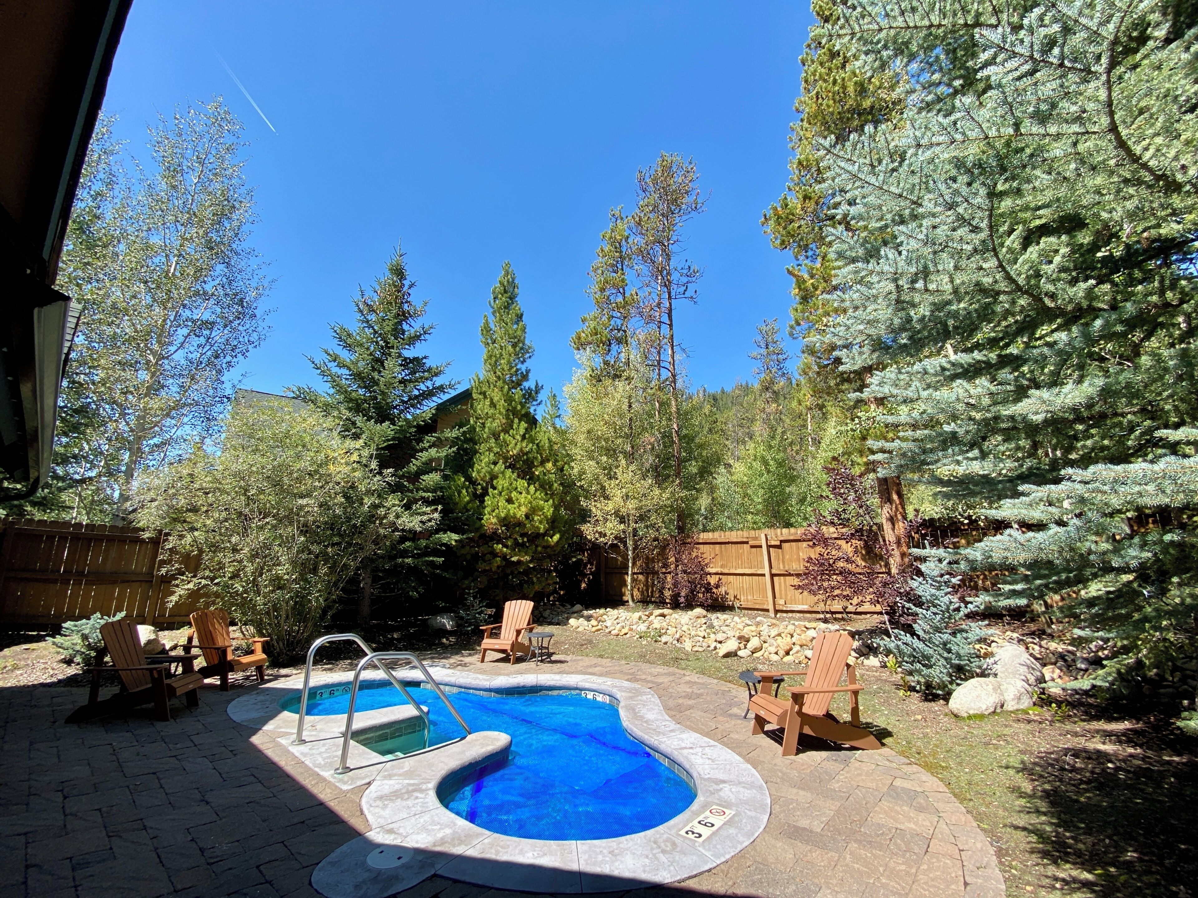 Patio con piscina, terraza de madera y árboles circundantes.