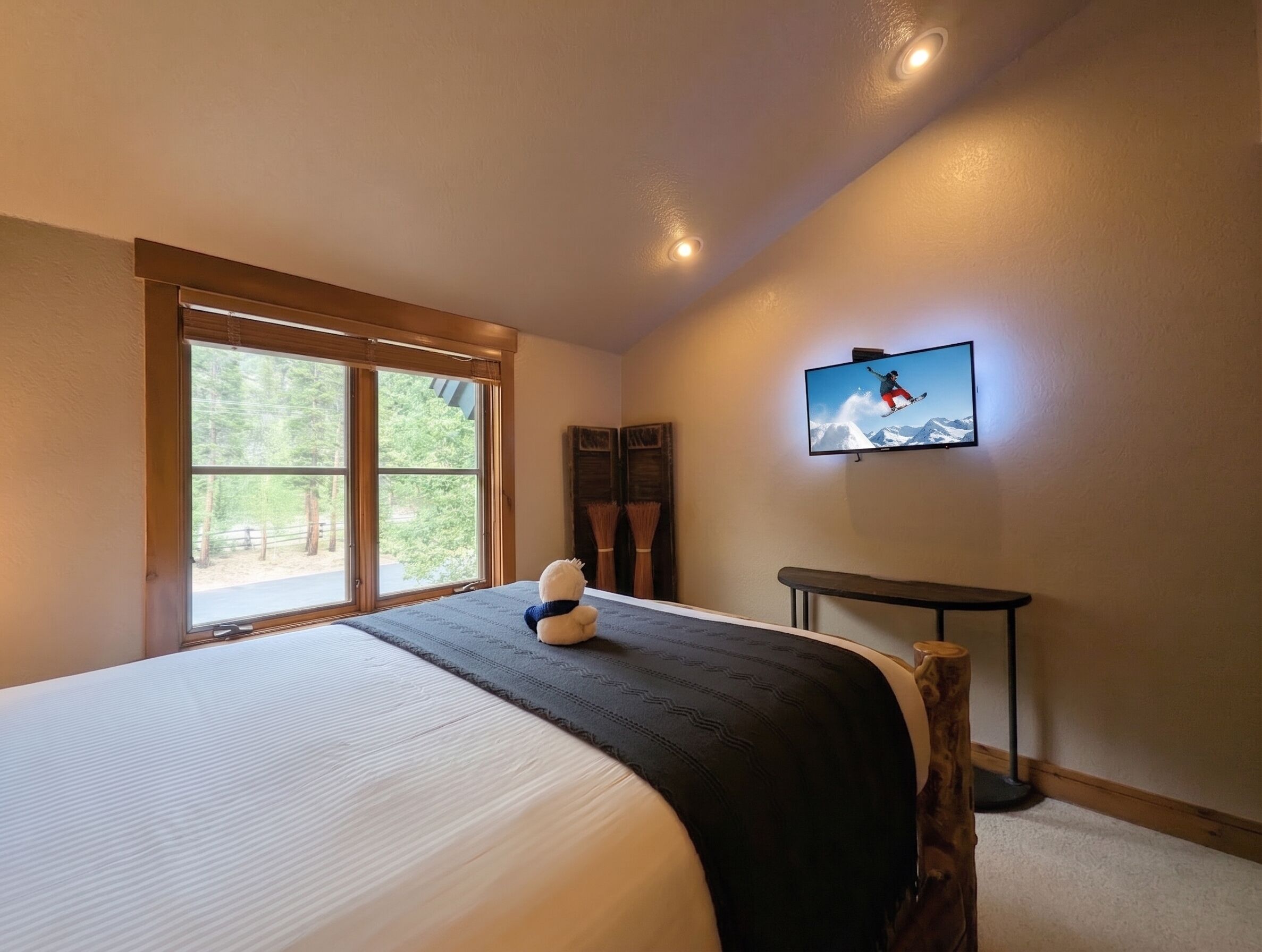 A bedroom with a large bed, a television mounted on the wall, and a window with a view of trees.