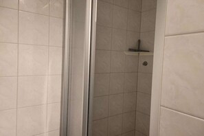 A bathroom with a shower area, tiled walls, and a small shelf. - Holiday apartment Strandstraße 42 322219 (Kühlungsborn)