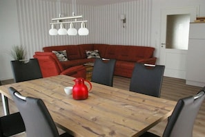 Ein Essbereich mit einem Holztisch, roten und schwarzen Stühlen, einer roten Karaffe und einem roten Sofa mit gemusterten Kissen.