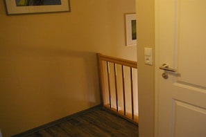 Ein Korridor mit Holzgeländer, einer weißen Tür und einem Lichtschalter an der Wand.
