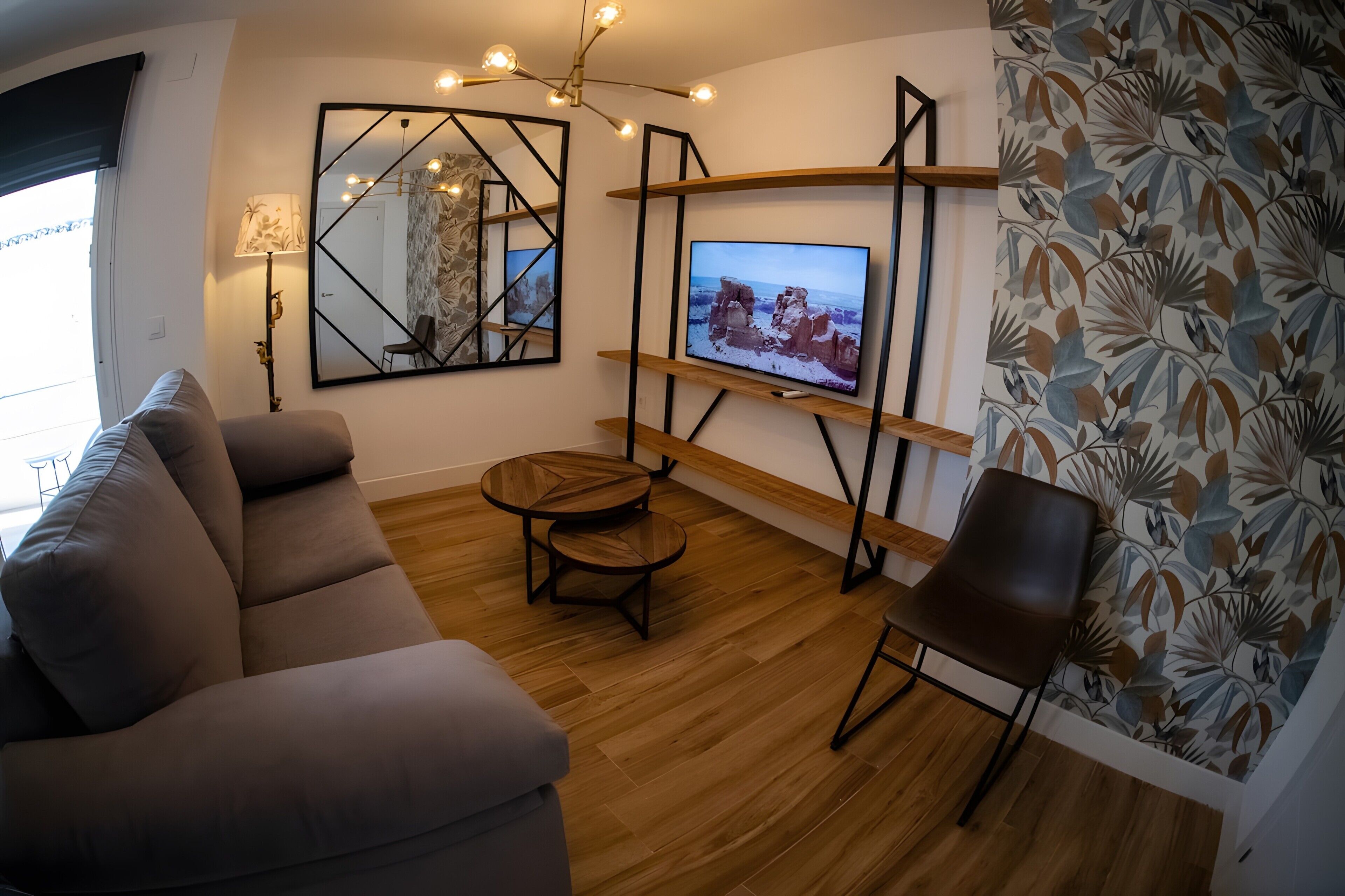 A living room with a sofa, a round coffee table, a TV on a stand, and a patterned wall.
