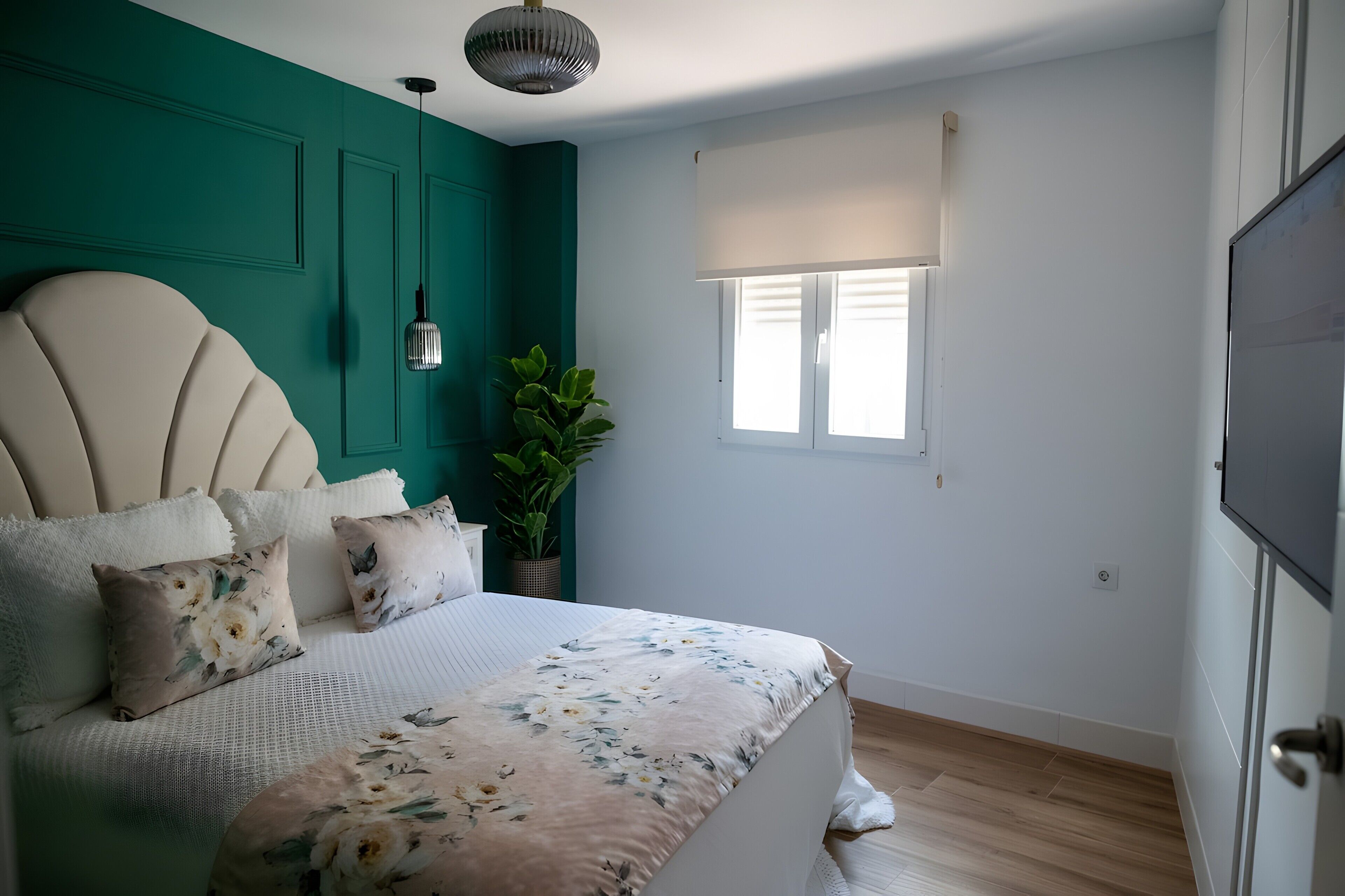 A bedroom with a bed, a potted plant, a window with blinds, and a door.