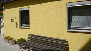 A yellow building with a bench outside, two windows, and a small lantern. - Holiday home in Oberfell with swimming pool (Oberfell)