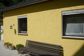 Ein gelbes Gebäude mit einer Bank vor der Fassade, zwei Fenstern und einem kleinen Laternen.