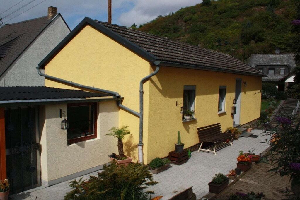A yellow building with a sloped roof, a front porch with a bench, and potted plants.