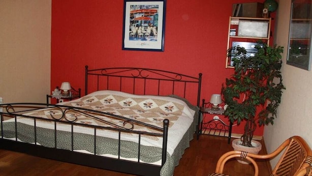 A bedroom with a metal bed frame, a bedside table with a lamp, a potted plant, and a framed picture on the wall. - Holiday home in Oberfell with swimming pool (Oberfell)