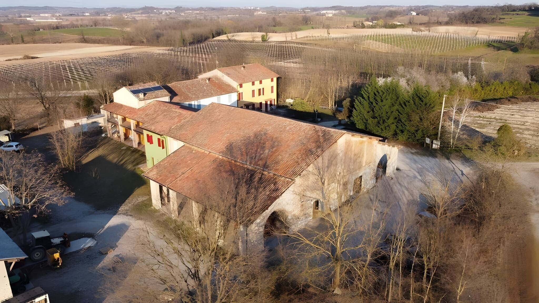 A rural property with a large building, a vineyard, and a stone bridge.