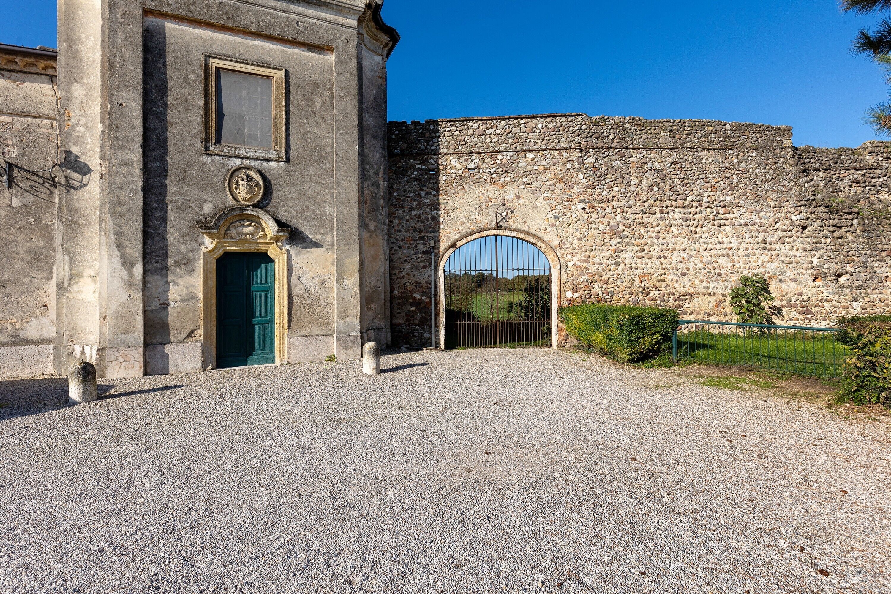 A historic building with a gravel driveway, a green door, and a stone wall.