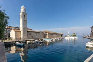 Ein historisches Gebäude mit einem Glockenturm, einer Uferpromenade und einer Reihe von Booten, die an der Kaimauer liegen.