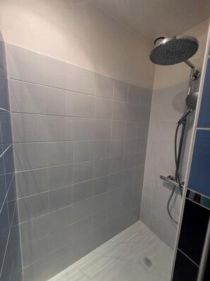 A shower with a handheld showerhead, a wall-mounted control panel, and a floor drain. - Vrbo Property (Versailles)