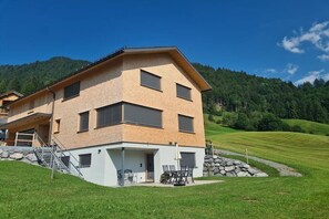 A multi-story building with a flat roof, a balcony, and a stone wall. - Holiday apartment with 2 bedrooms (Au im Bregenzerwald)