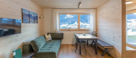 A cozy room with a sofa, a dining table, and a window with a view of mountains.