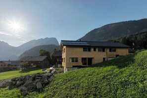 A modern two-story house with a sloped roof, solar panels, and a stone wall in the foreground. - Holiday apartment with 2 bedrooms (Au im Bregenzerwald)