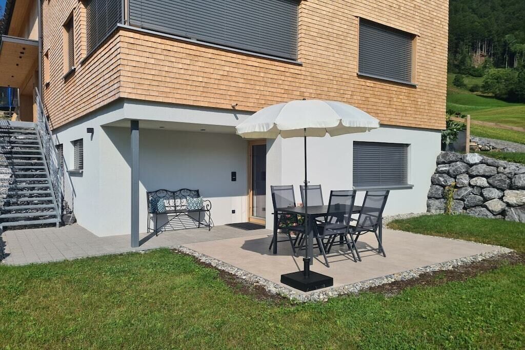 Een modern huis met een terras, buitenmeubels en een stenen muur.