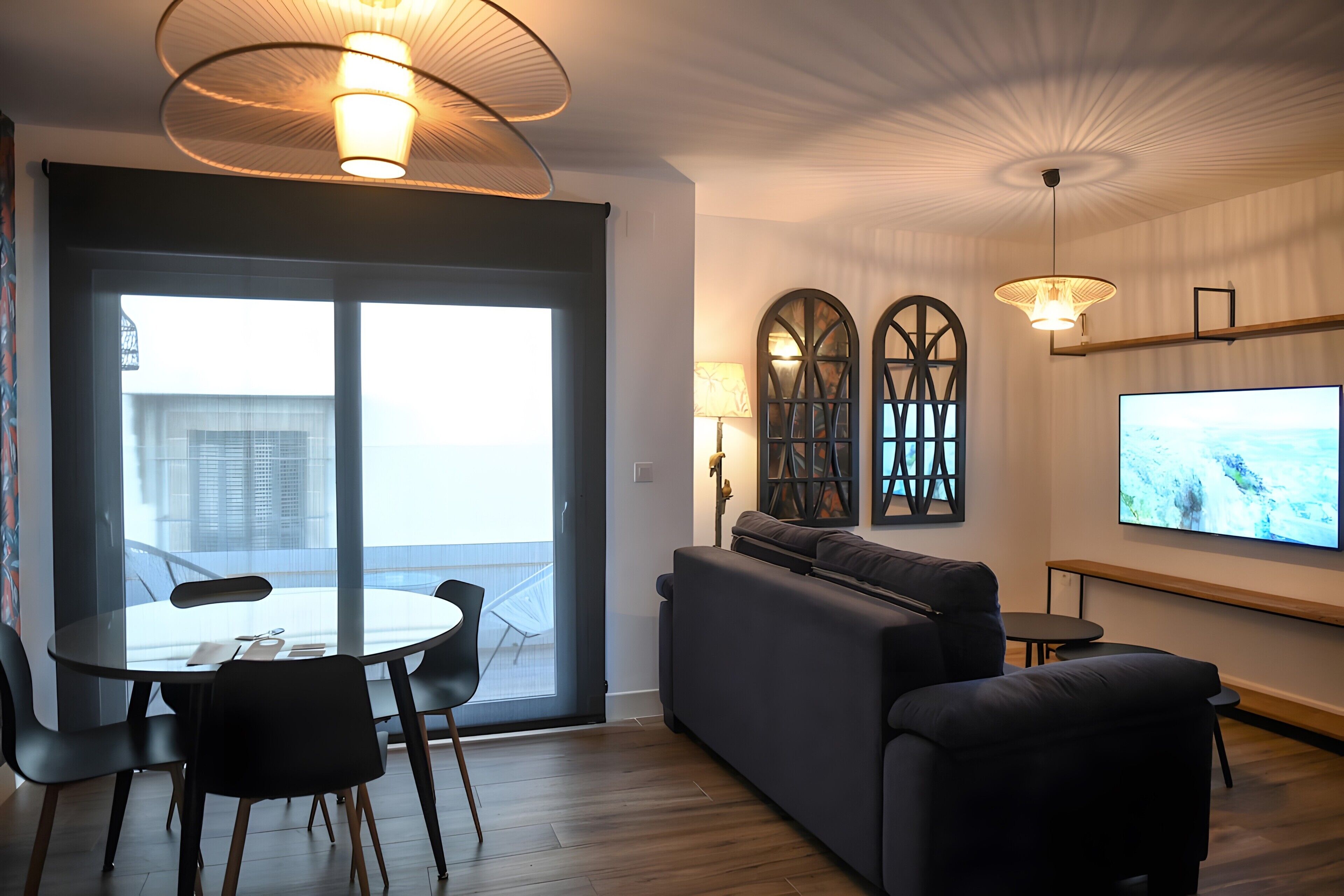 A modern living room with a sofa, a dining table with chairs, and a television on the wall.