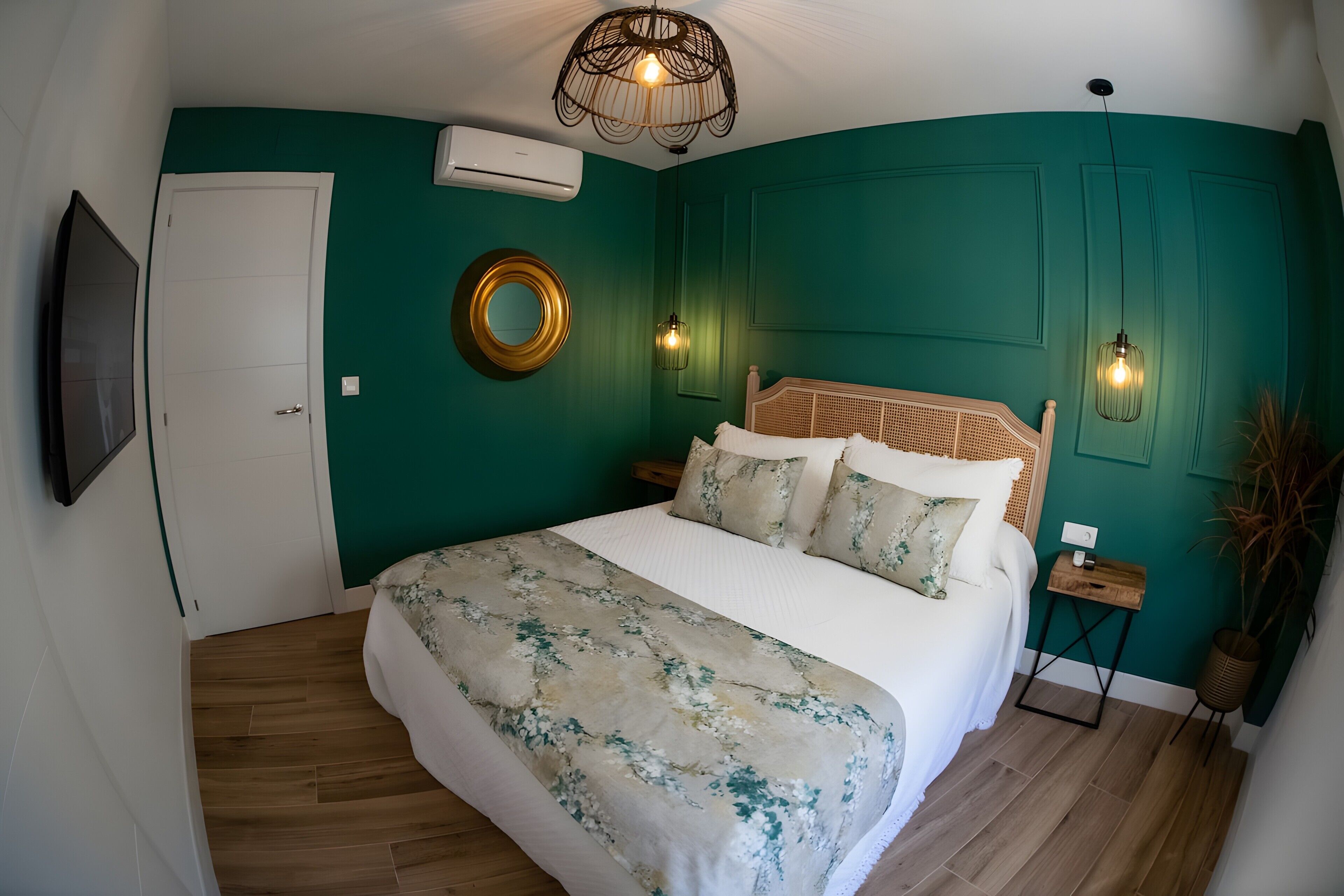 Une chambre à coucher comprenant un lit, un téléviseur fixé au mur, un miroir rond et un luminaire au plafond.