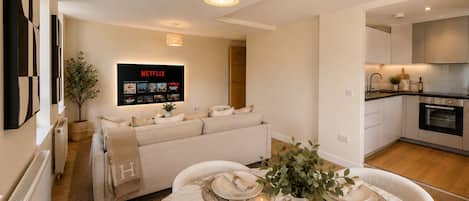 A modern living room with a sofa, a dining table set for four, and a kitchen area with cabinets and appliances.