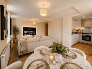 Ein modernes Wohnzimmer mit einer Couch, einem Esstisch für vier Personen und einer Küchenzeile mit Schränken und Geräten.