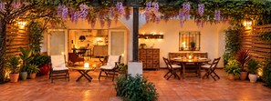 An outdoor patio with a dining table and chairs, surrounded by potted plants and a wooden pergola with hanging vines. - Charming Getaway for 2 with a Veranda & Pool | Conil. (Conil de la Frontera)