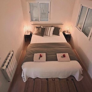 A bedroom with a bed, two bedside tables, a radiator, and a window with blinds. - Charming Getaway for 2 with a Veranda & Pool | Conil. (Conil de la Frontera)