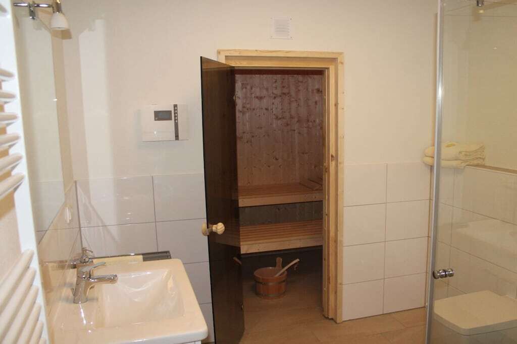 Et badeværelse med en hvid vask, et brusekabine med glas, og en trædør, der fører til bruseafsnittet.