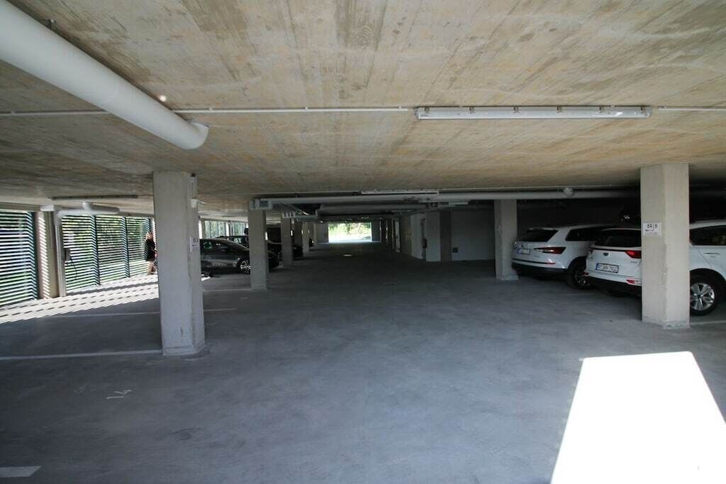 Un parking avec des piliers en béton, un plafond plat et plusieurs voitures garées.