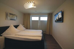 A hotel room with a bed, a nightstand, a ceiling light fixture, a window with curtains, and a wall-mounted picture. - Holiday apartment with 2 bedrooms (Cuxhaven)