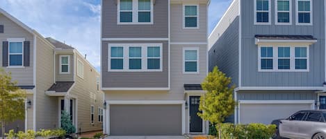 A multi-story residential building with a central garage, a driveway, and a car parked in the driveway.