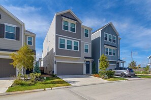 A residential street with modern two-story houses, a clear sky, and a parked car.